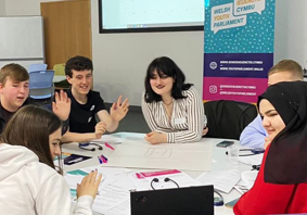 A group of young people sat around a table talking to each other.