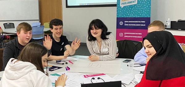 A group of young people sat around a table talking to each other.